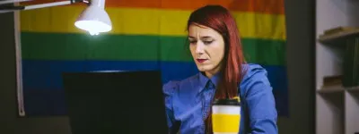 Person working on their computer in front of a LGBTQ+ flag